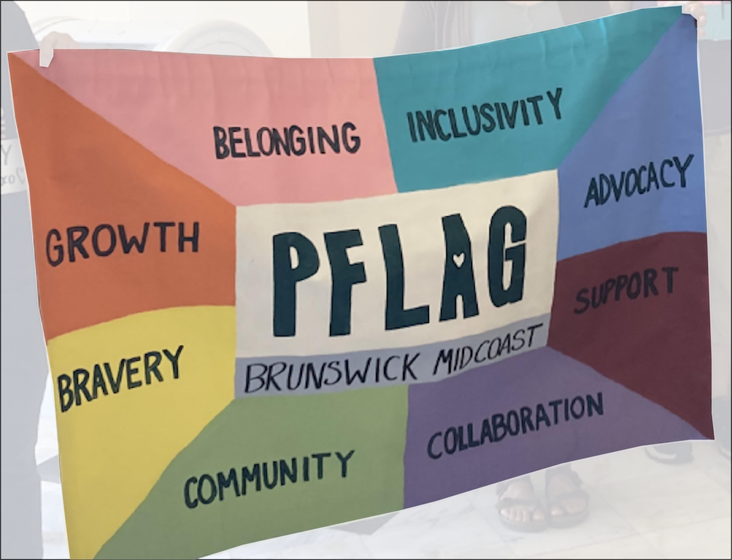 PFLAG members hold up a banner, which reads: "PFLAG Brunswick/Midcoast; Belonging, Inclusivity, Advocacy, Support, Collaboration, Community, Bravery, Growth."